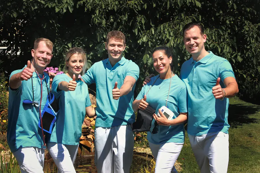 Fünf Mitarbeitende von Pflege Dorn in türkisfarbenen Poloshirts zeigen im Garten den Daumen nach oben